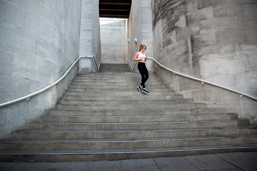 Corredor ejecutando stair running en escaleras deportivas con técnica de antepié y postura erguida